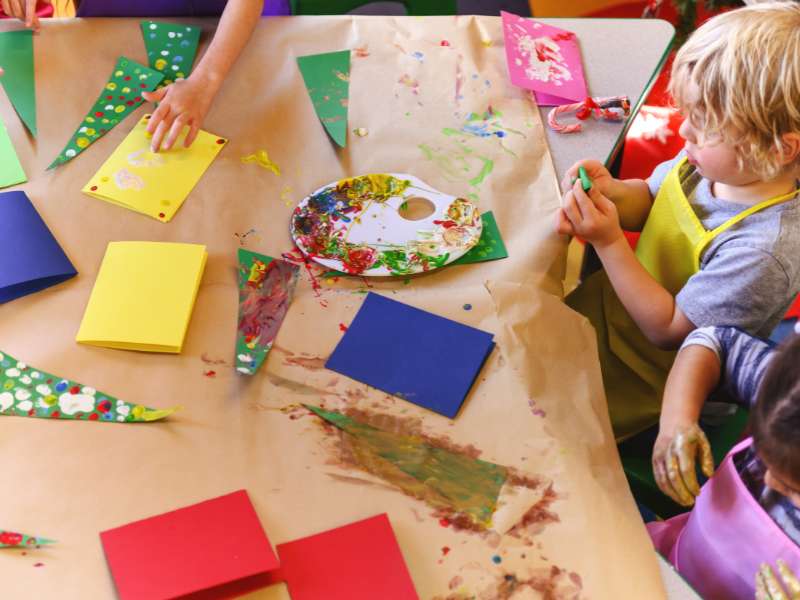 “Enfant décorant l’ange en assiette en carton avec peinture et paillettes.”