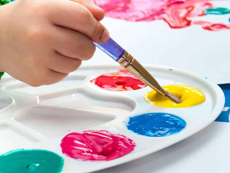 Enfant peignant un rouleau cartonné en blanc pour fabriquer un bonhomme de neige DIY.