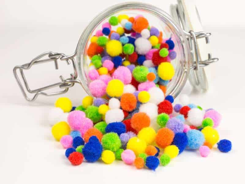 Pompons colorés et fil chenille collés sur un rouleau pour décorer un bonhomme de neige.